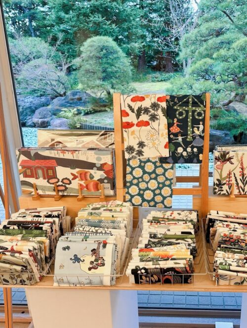 スウェーデン・テキスタイル展のポスターと、特設ショップに並ぶ花柄や動物柄の北欧生地・カットクロス・バッグ・雑貨