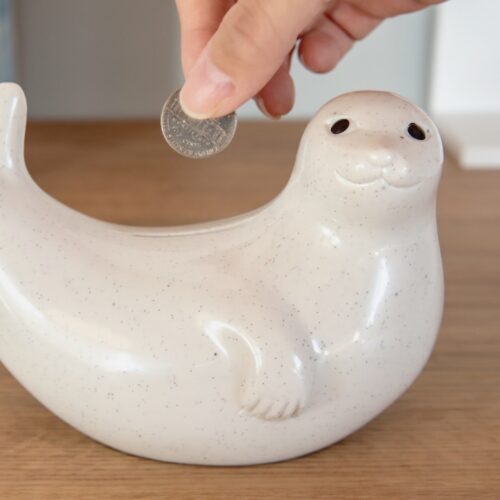 クリーム色の陶器製アザラシ貯金箱。イエローとホワイトのニットマフラー付き、フィンランド産北欧雑貨